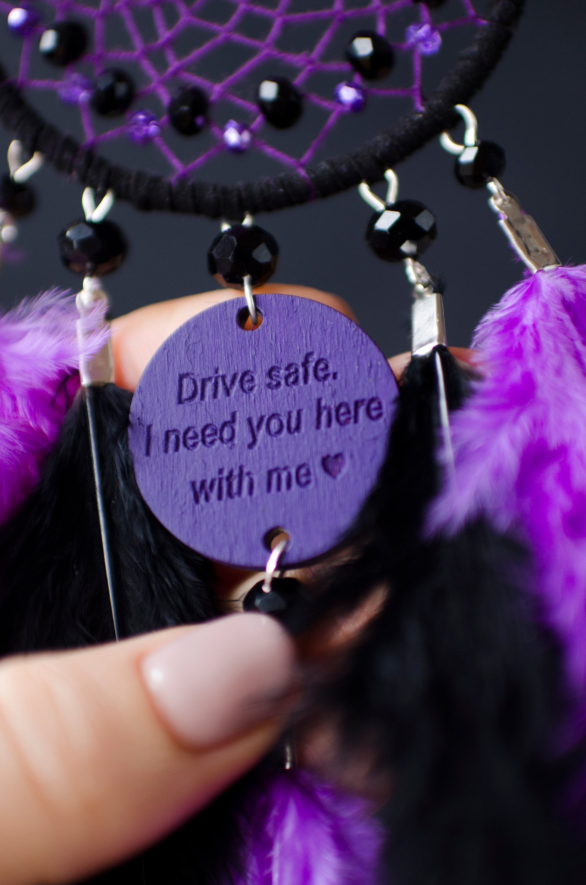 Handcrafted purple and black dream catcher with beaded web design, adorned with vibrant feathers. The centerpiece includes a charm with an engraved message, making it a thoughtful gift or car accessory.