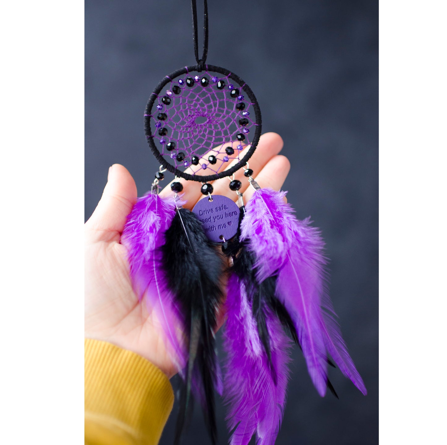 Handcrafted purple and black dream catcher with beaded web design, adorned with vibrant feathers. The centerpiece includes a charm with an engraved message, making it a thoughtful gift or car accessory.