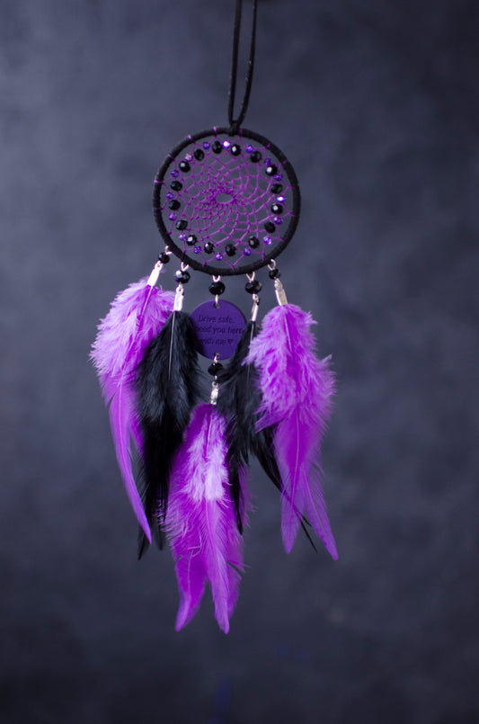 Handcrafted purple and black dream catcher with beaded web design, adorned with vibrant feathers. The centerpiece includes a charm with an engraved message, making it a thoughtful gift or car accessory.