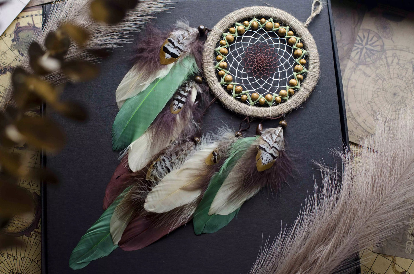 Handmade dream catcher with a 6-inch hoop wrapped in natural jute twine, featuring an intricate web design with wooden beads. Adorned with an array of feathers in green, cream, and brown tones, it serves as a beautiful boho wall decor piece. Perfect for adding a touch of rustic charm to any room.