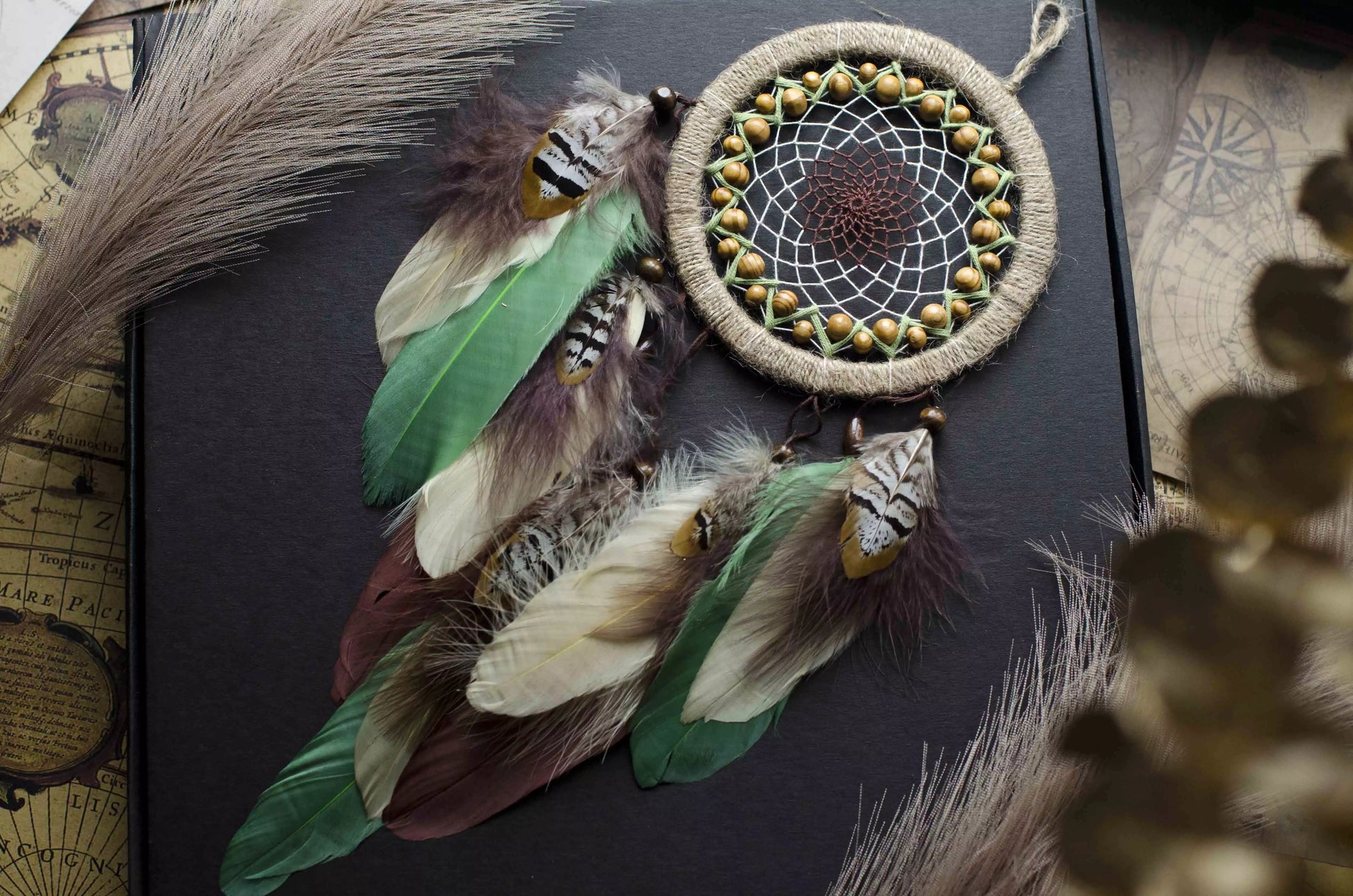 Handmade dream catcher with a 6-inch hoop wrapped in natural jute twine, featuring an intricate web design with wooden beads. Adorned with an array of feathers in green, cream, and brown tones, it serves as a beautiful boho wall decor piece. Perfect for adding a touch of rustic charm to any room.