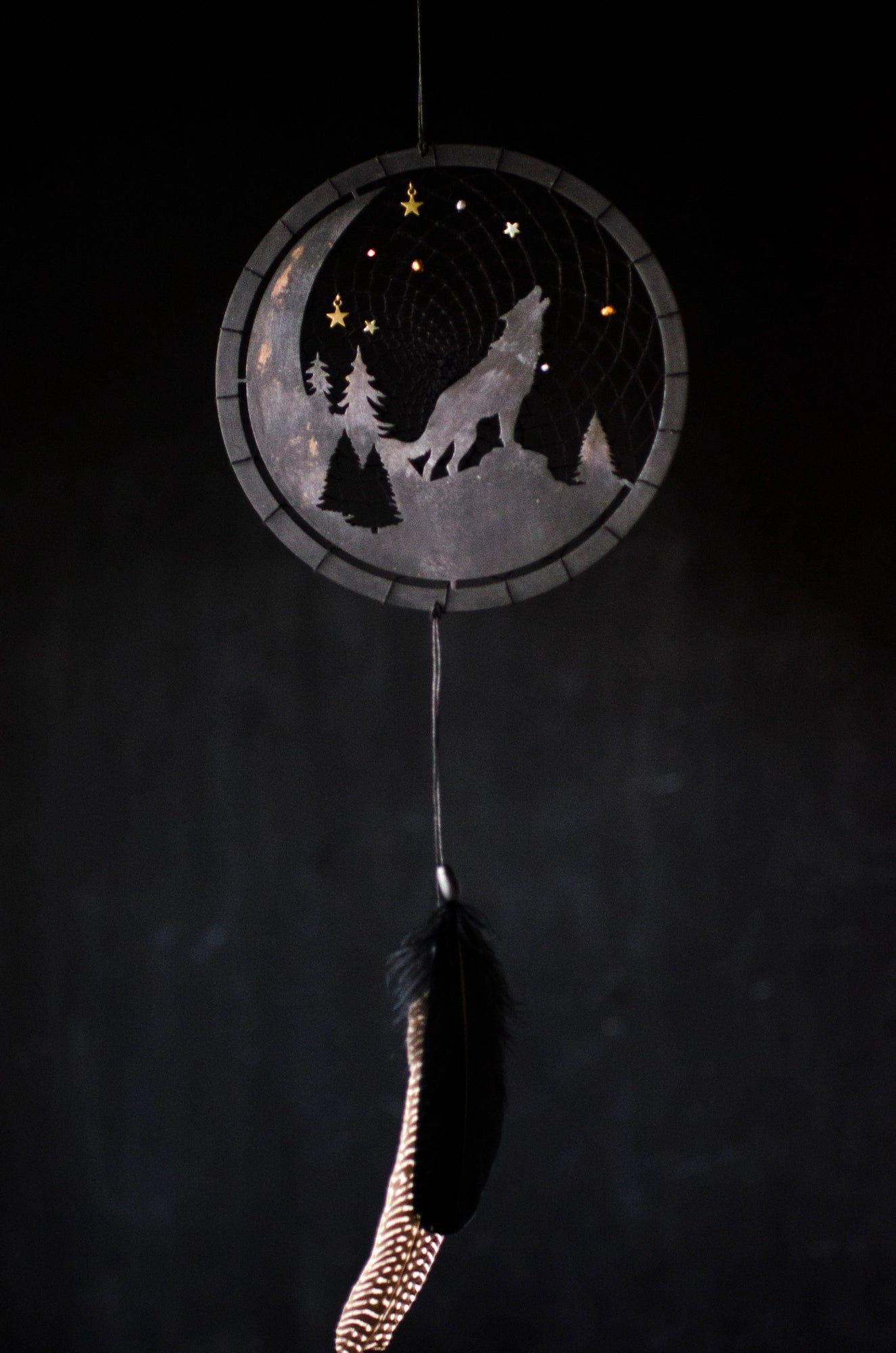 A handcrafted dream catcher with a howling wolf silhouette, moon, and forest design. Decorated with star-shaped beads, this unique piece captures the essence of the night. The hoop measures approximately 8 inches in diameter, featuring black and natural shades.