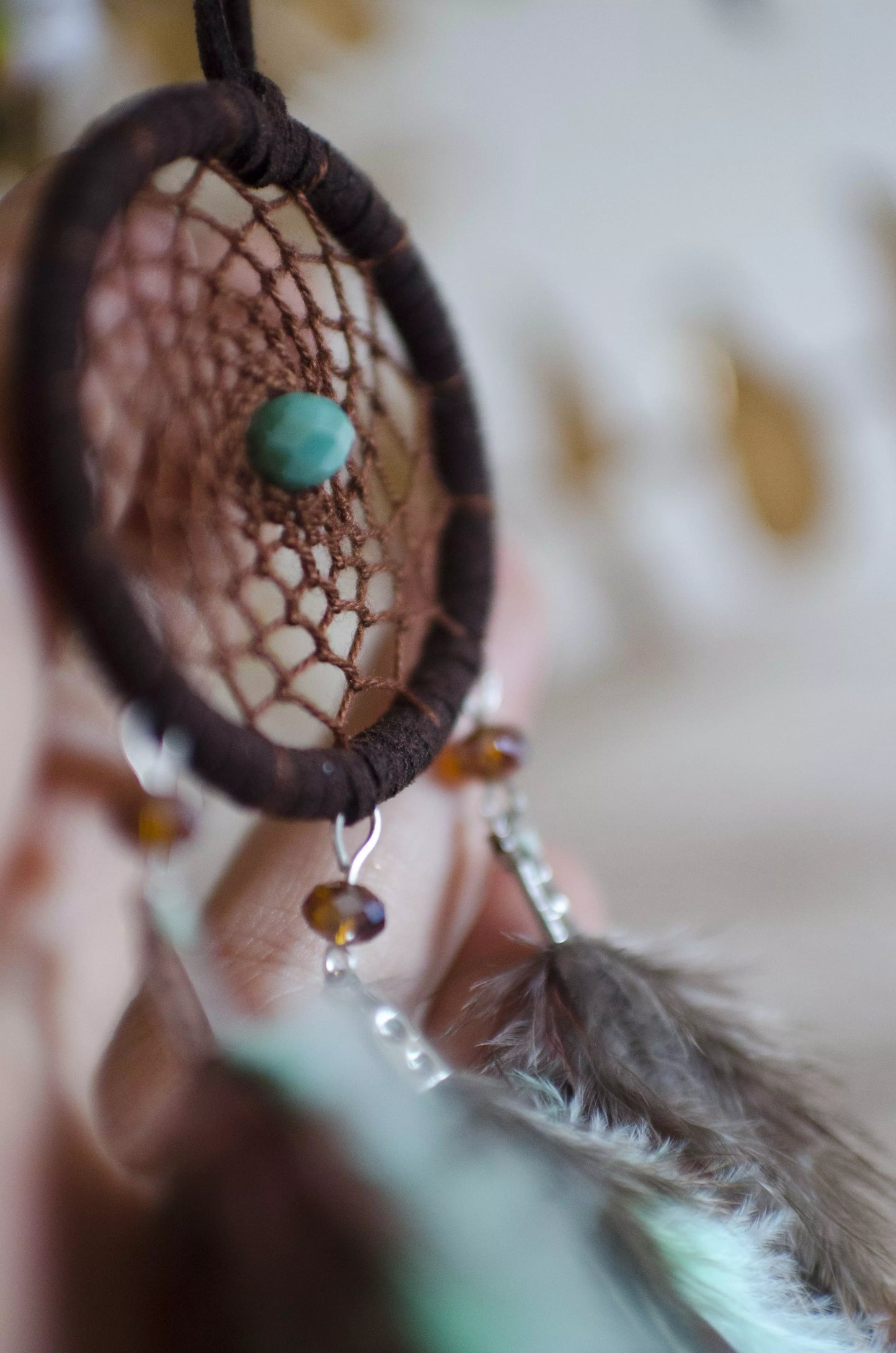 Handmade small dreamcatcher featuring a brown web, turquoise stone center, and brown and mint green feathers, perfect as boho car decor or for adding positive energy and protection to any space.