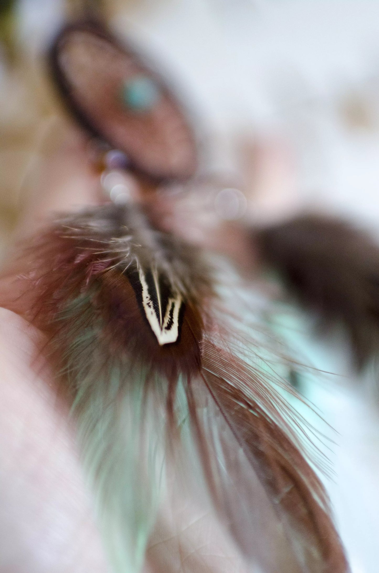 Handmade small dreamcatcher featuring a brown web, turquoise stone center, and brown and mint green feathers, perfect as boho car decor or for adding positive energy and protection to any space.