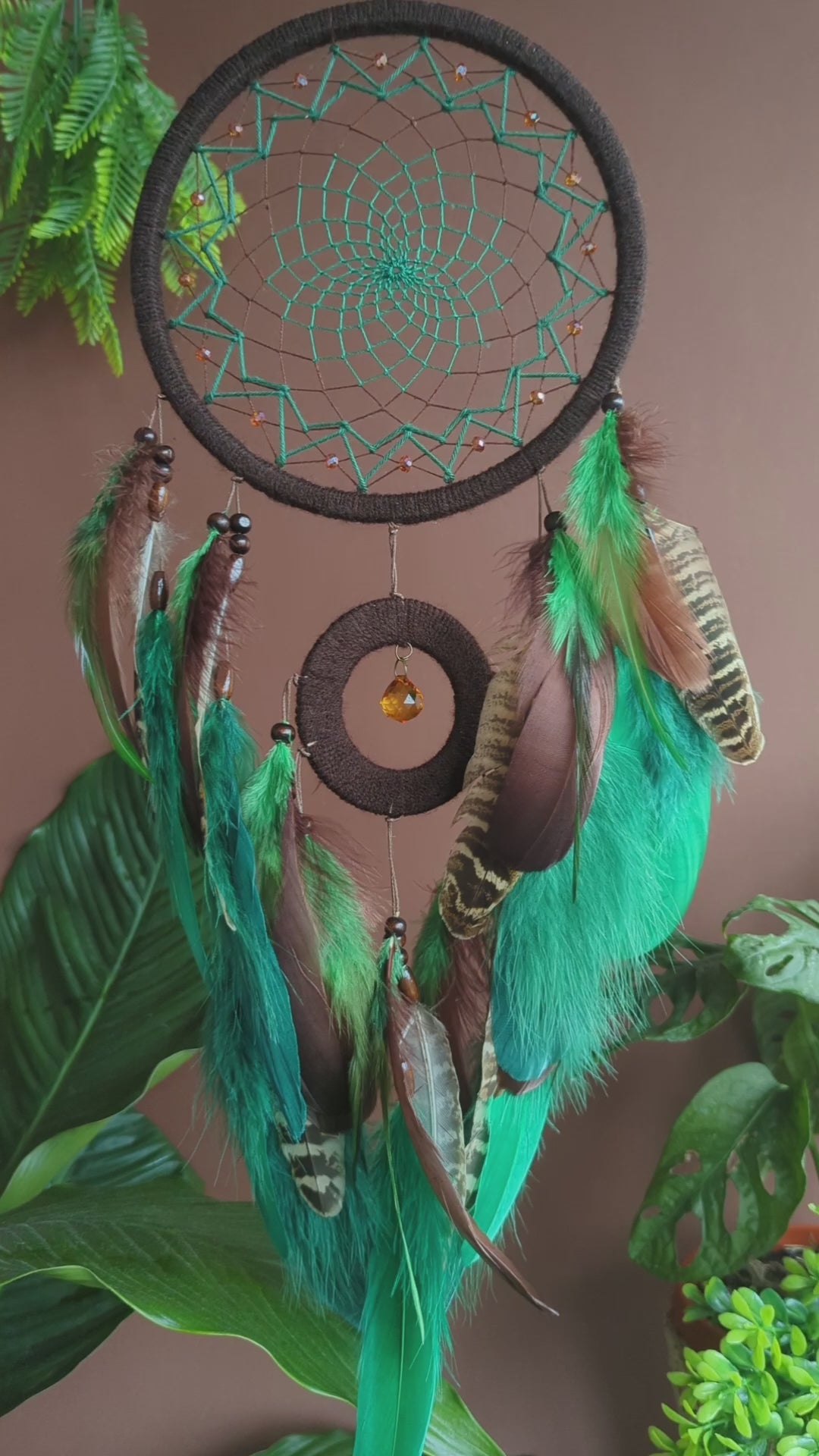 Handcrafted green dream catcher with a faceted amber crystal and natural feathers, featuring an intricate web design and earthy tones. Perfect for home decor or as a spiritual protection gift.