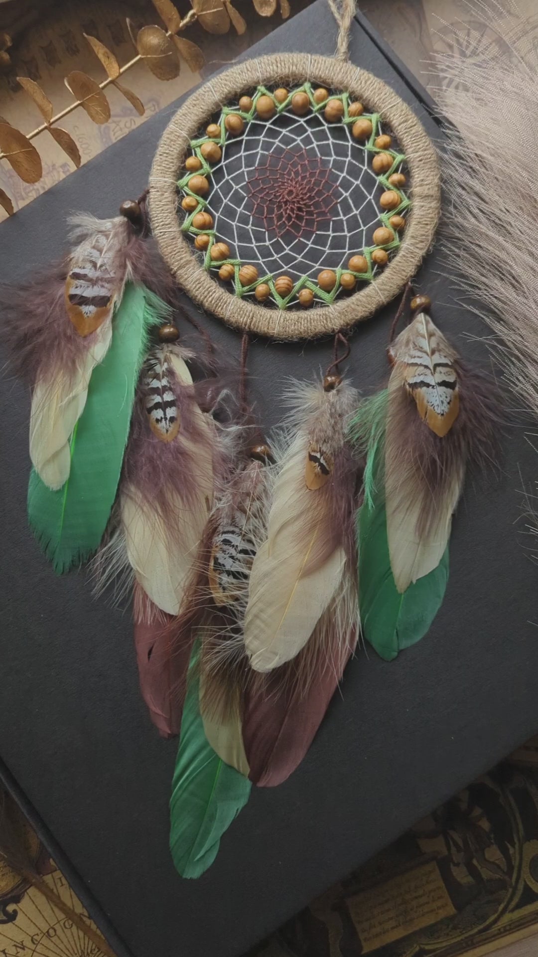 Handmade dream catcher with a 6-inch hoop wrapped in natural jute twine, featuring an intricate web design with wooden beads. Adorned with an array of feathers in green, cream, and brown tones, it serves as a beautiful boho wall decor piece. Perfect for adding a touch of rustic charm to any room.