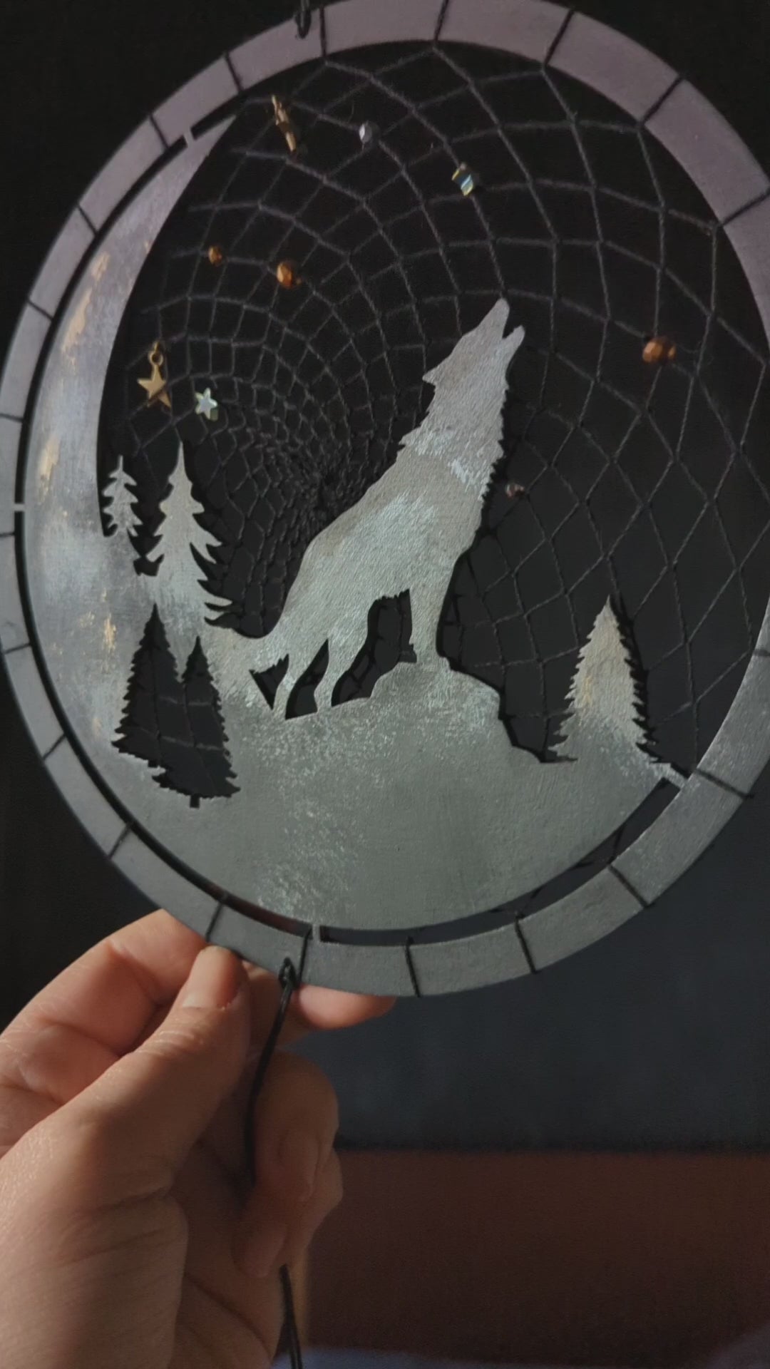 A handcrafted dream catcher with a howling wolf silhouette, moon, and forest design. Decorated with star-shaped beads, this unique piece captures the essence of the night. The hoop measures approximately 8 inches in diameter, featuring black and natural shades.