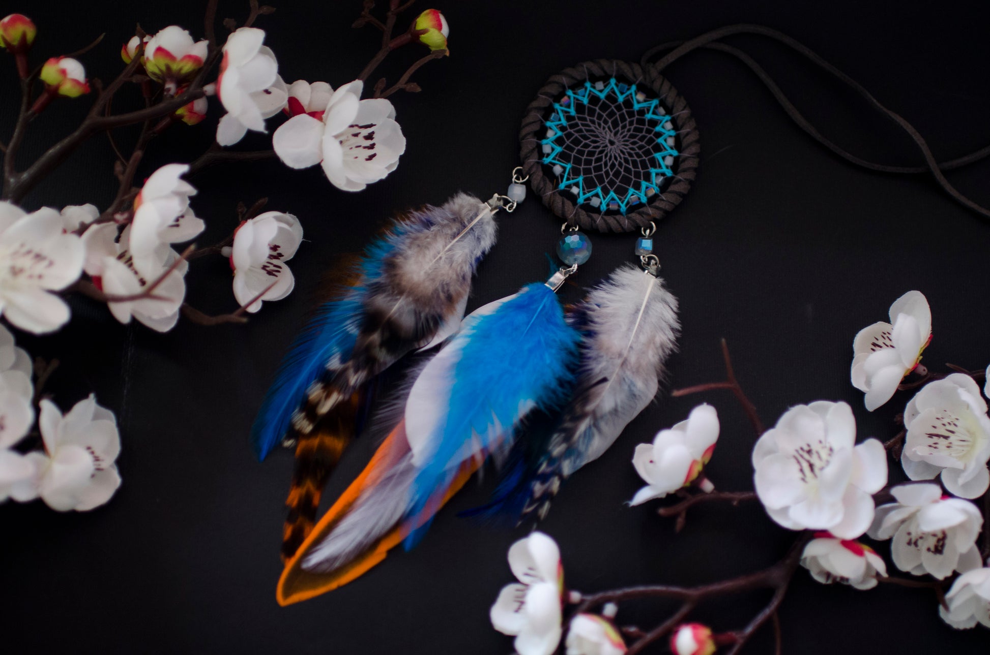 Small dreamcatcher for car in shades of gray, turquoise, blue, and orange. Features intricate webbing with a central turquoise bead, surrounded by feathers and beads in coordinating colors. Perfect for adding a touch of boho charm to your vehicle