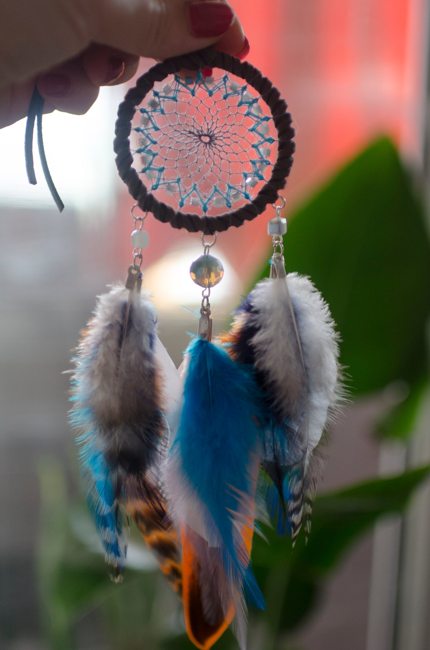 Small dreamcatcher for car in shades of gray, turquoise, blue, and orange. Features intricate webbing with a central turquoise bead, surrounded by feathers and beads in coordinating colors. Perfect for adding a touch of boho charm to your vehicle