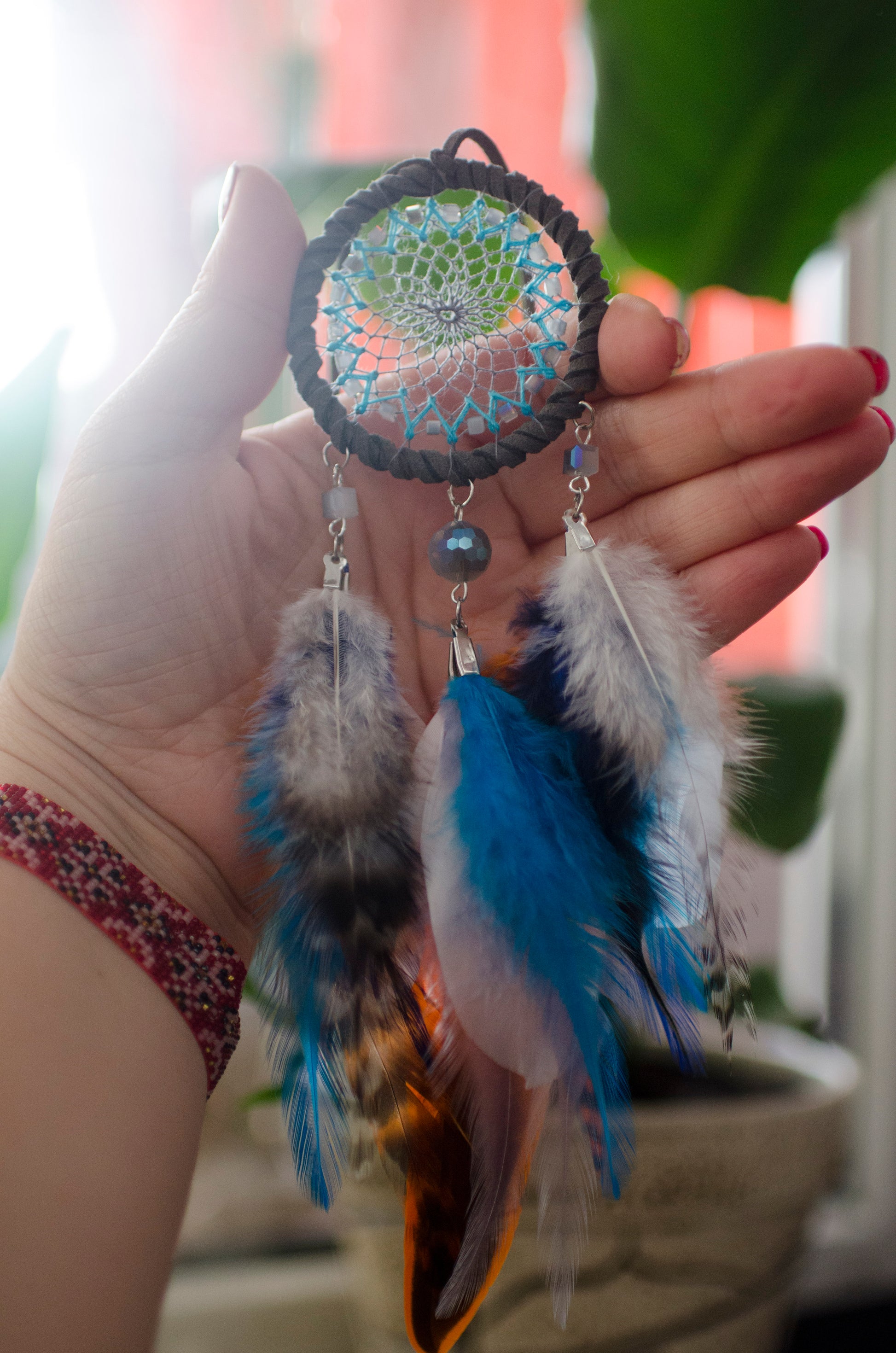 Small dreamcatcher for car in shades of gray, turquoise, blue, and orange. Features intricate webbing with a central turquoise bead, surrounded by feathers and beads in coordinating colors. Perfect for adding a touch of boho charm to your vehicle