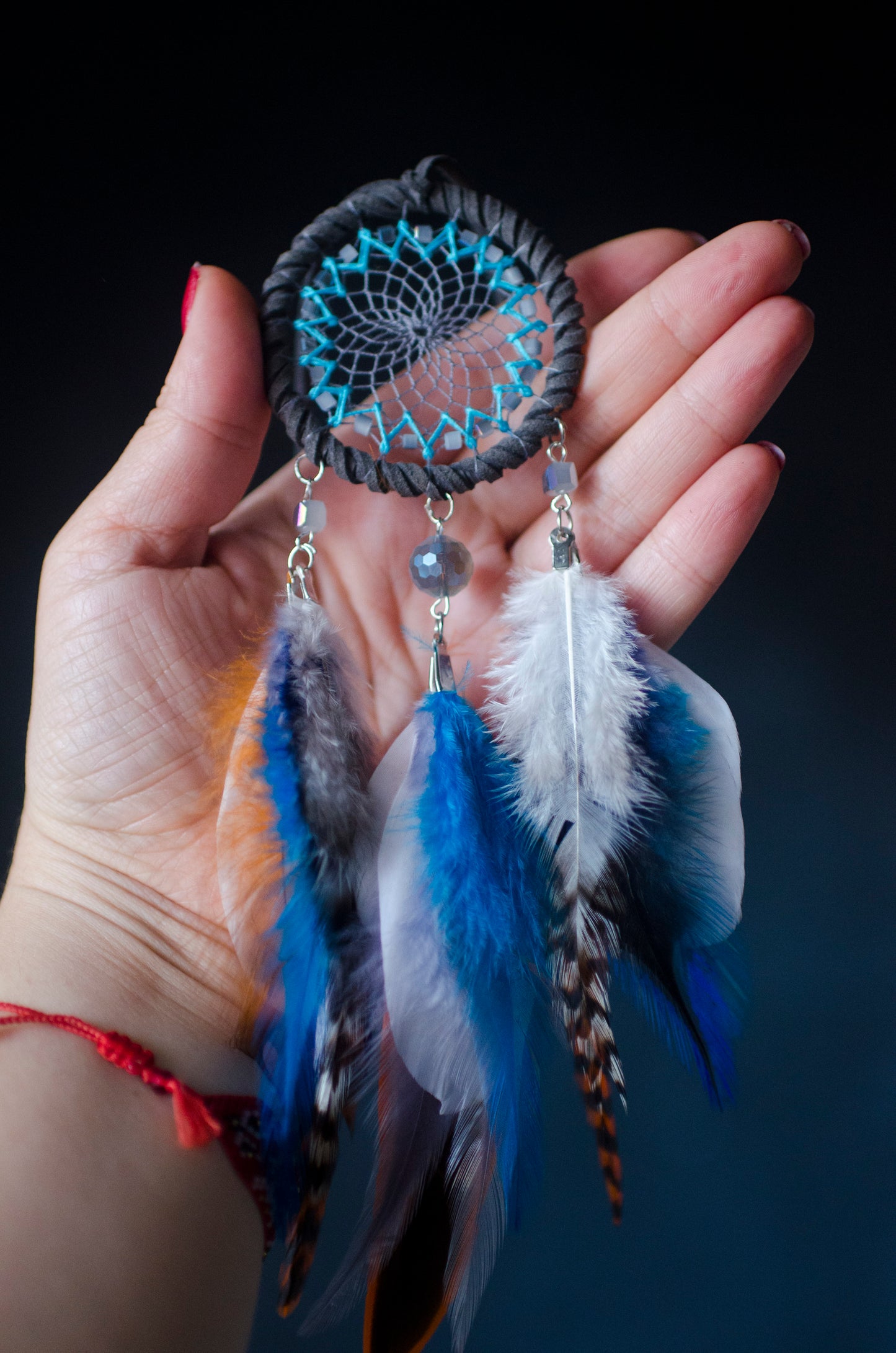 Small dreamcatcher for car in shades of gray, turquoise, blue, and orange. Features intricate webbing with a central turquoise bead, surrounded by feathers and beads in coordinating colors. Perfect for adding a touch of boho charm to your vehicle