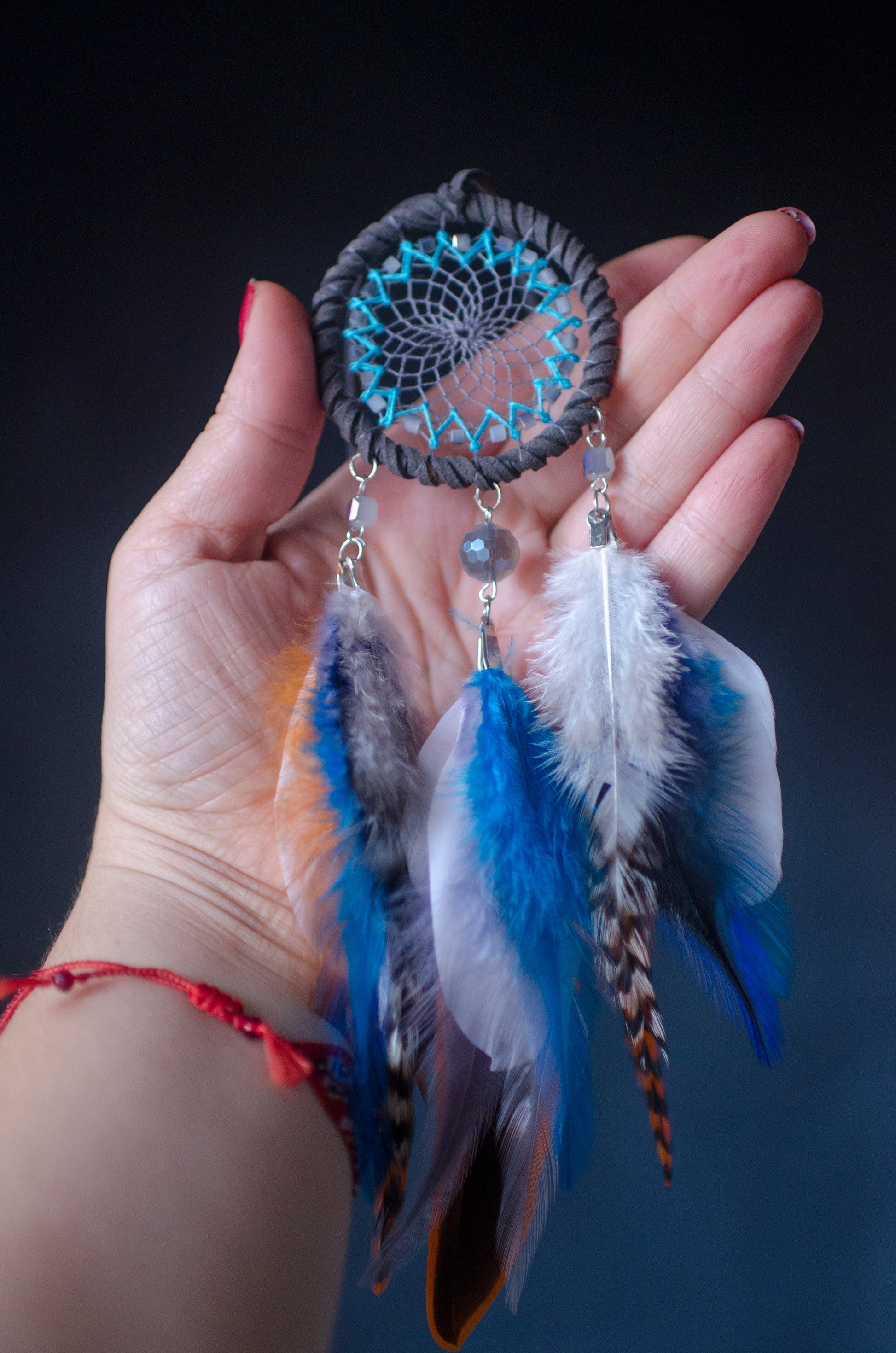 Small dreamcatcher for car in shades of gray, turquoise, blue, and orange. Features intricate webbing with a central turquoise bead, surrounded by feathers and beads in coordinating colors. Perfect for adding a touch of boho charm to your vehicle