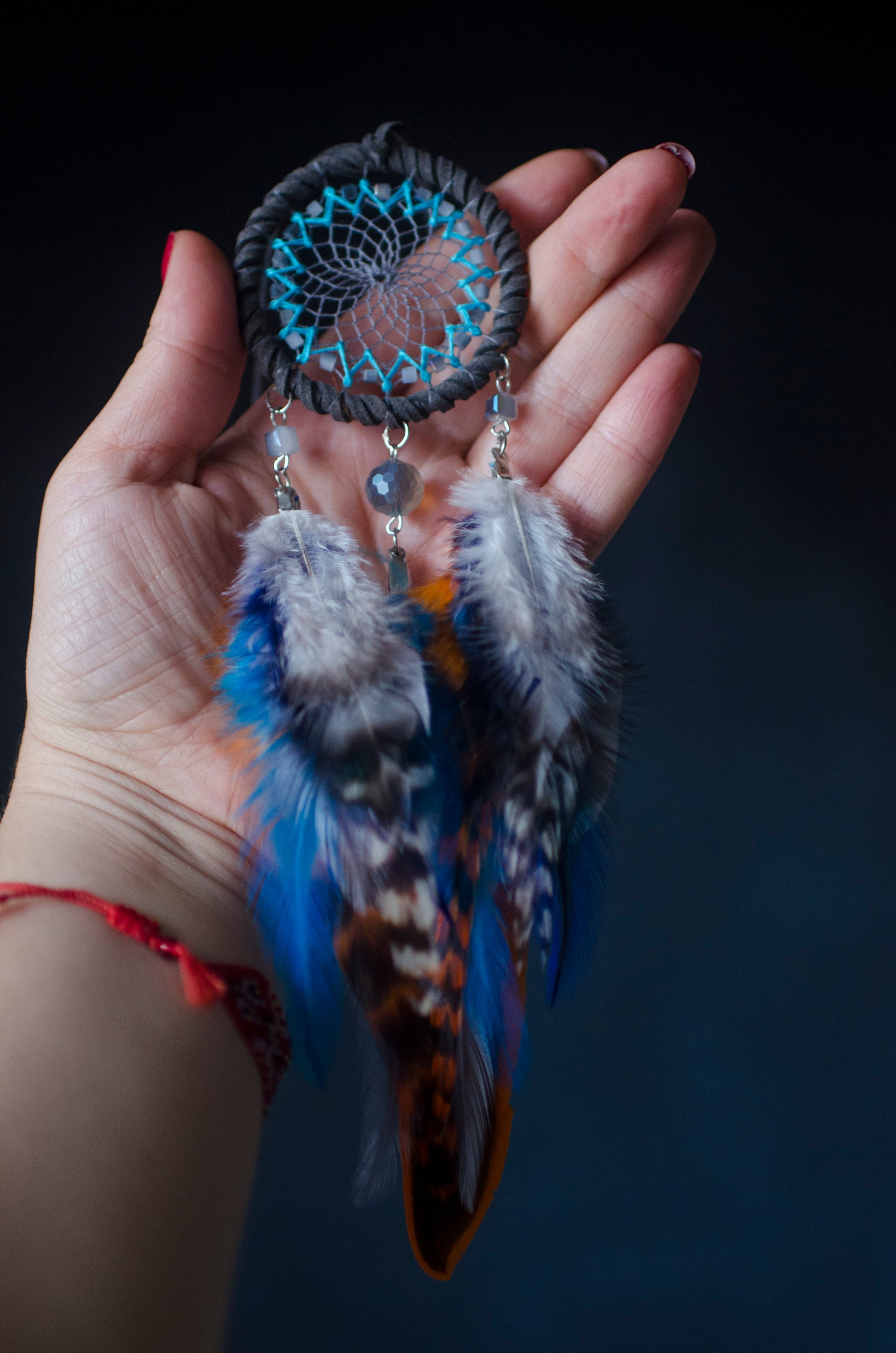 Small dreamcatcher for car in shades of gray, turquoise, blue, and orange. Features intricate webbing with a central turquoise bead, surrounded by feathers and beads in coordinating colors. Perfect for adding a touch of boho charm to your vehicle